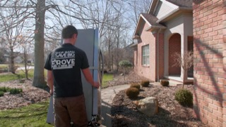 Delivery person from Grove Appliance carrying a new appliance to a brick house.